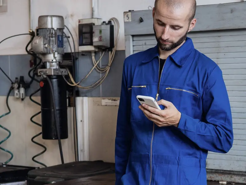An engineer in work overalls checking his phone.